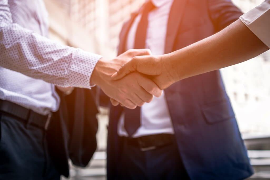 Two men shaking hands with a third standing behind.